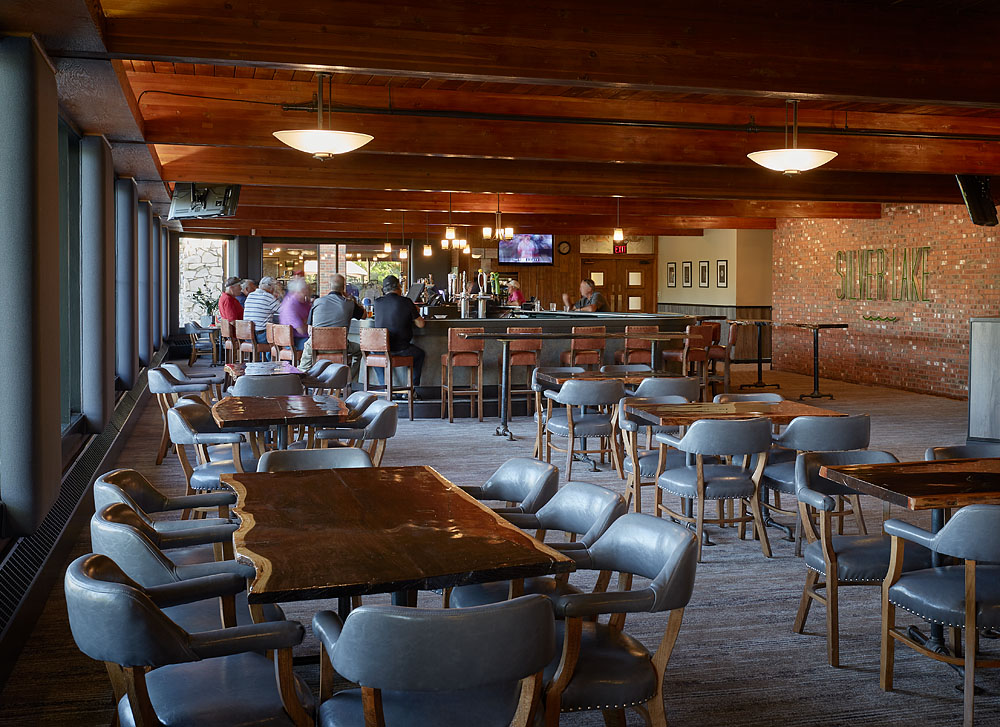 View from the dining room at the Silver Lake bar, with numerous tables and comfortable chairs while patrons drink and dine at the bar in the background.
