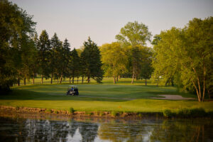 Golf cart drives along the water's edge at dusk.
