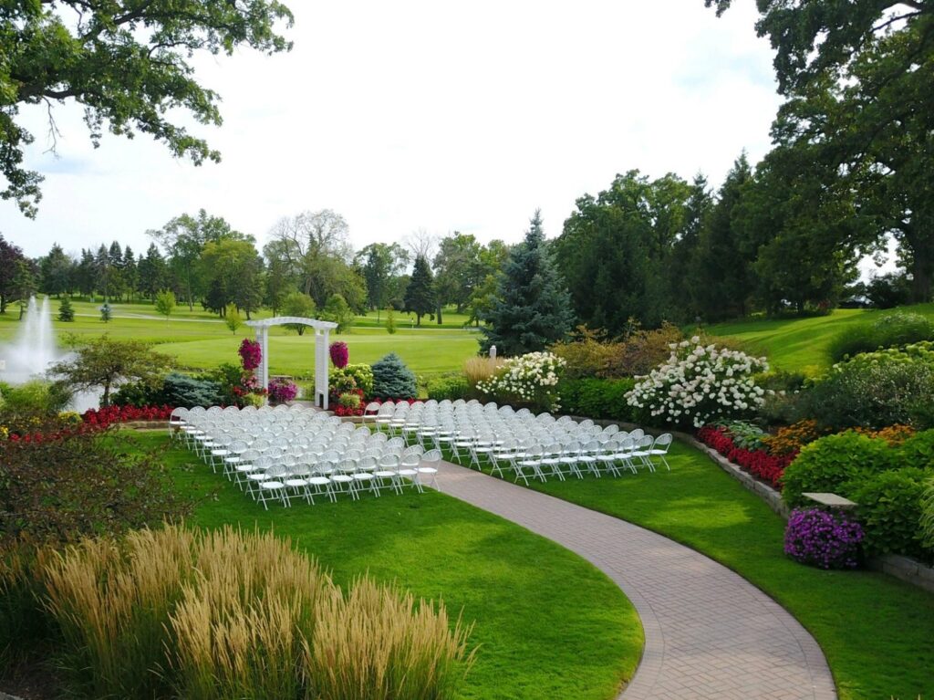 Perfectly manicured grass and flower bushes surround chairs and altar with the fountain in the background.